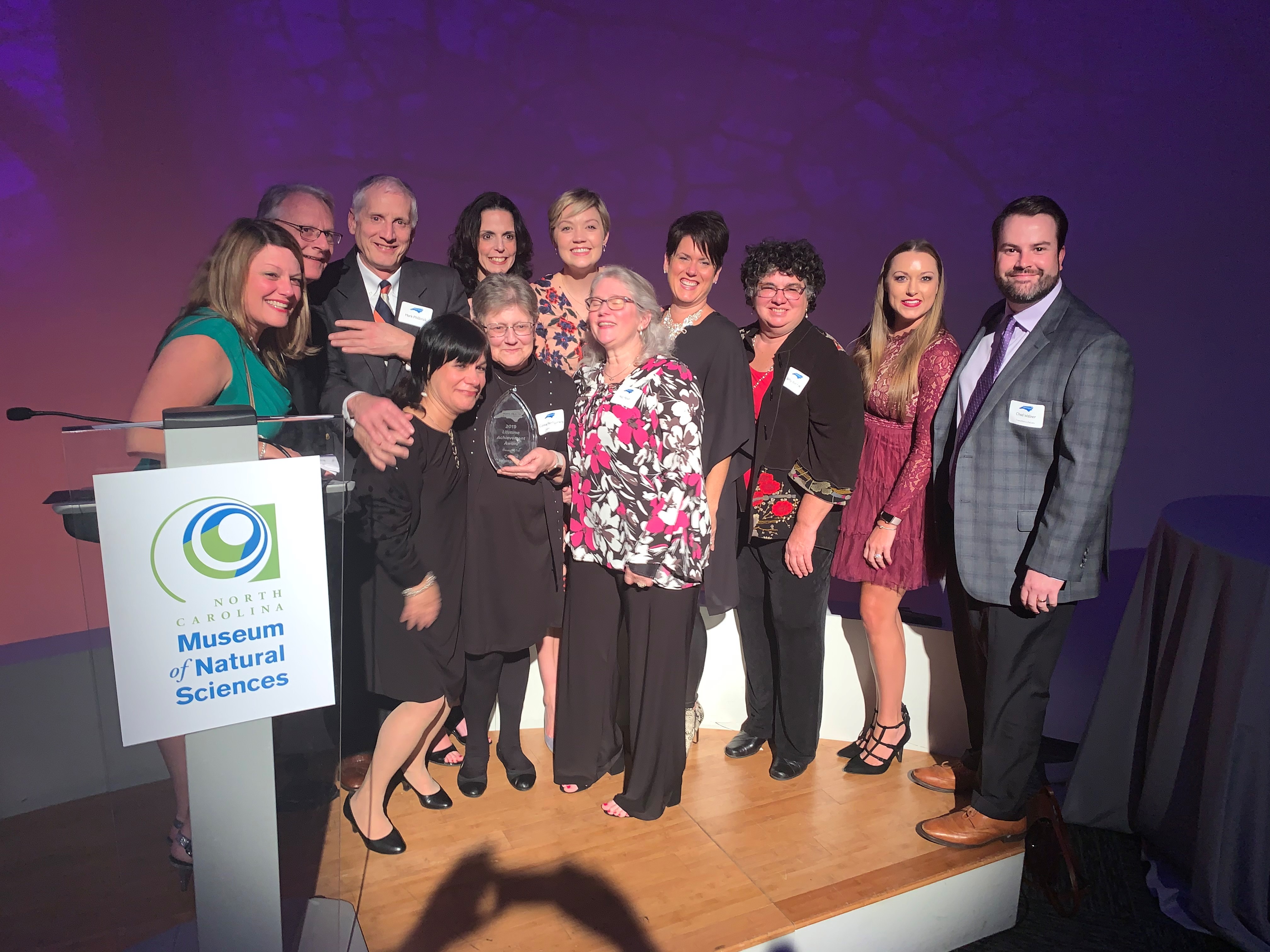 group of people hugging a woman at awards ceremony